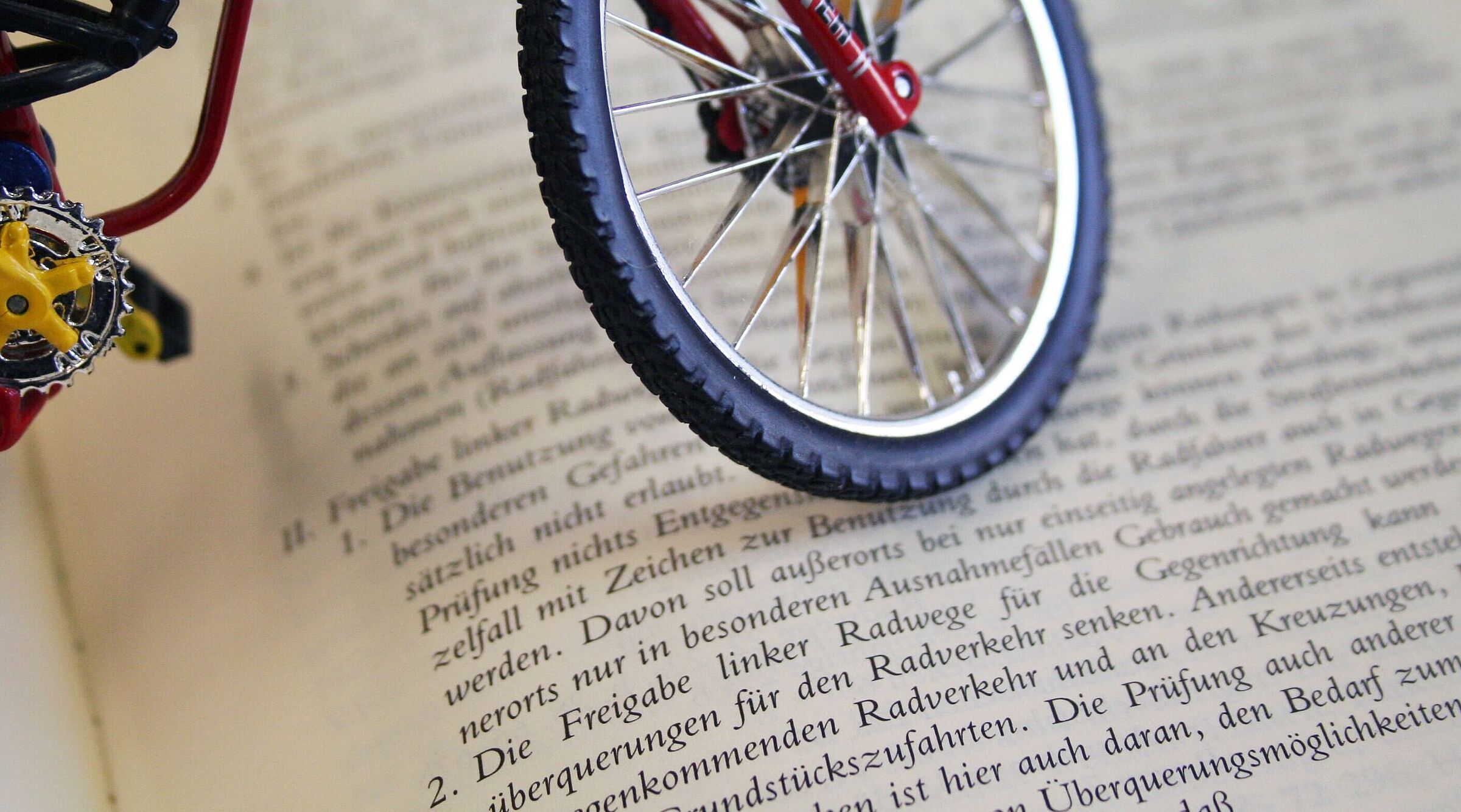 Miniatur-Fahrrad steht auf einem aufgeschlagenen Buch mit deutschem Gesetzestext.